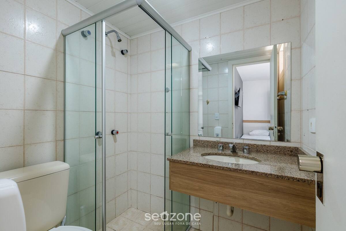 Een badkamer met een douche met glazen wanden, een wastafel met een houten kastje en een spiegel boven de wastafel.