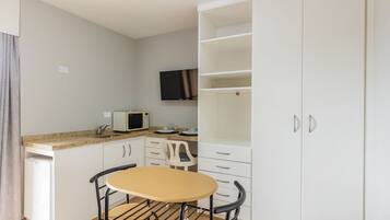 A compact kitchen with a microwave, white cabinets, a small table, and a TV mounted on the wall.