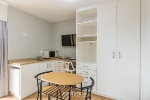 A compact kitchen with a microwave, white cabinets, a small table, and a TV mounted on the wall. - Studios at Upper Residence - UPP (Curitiba)