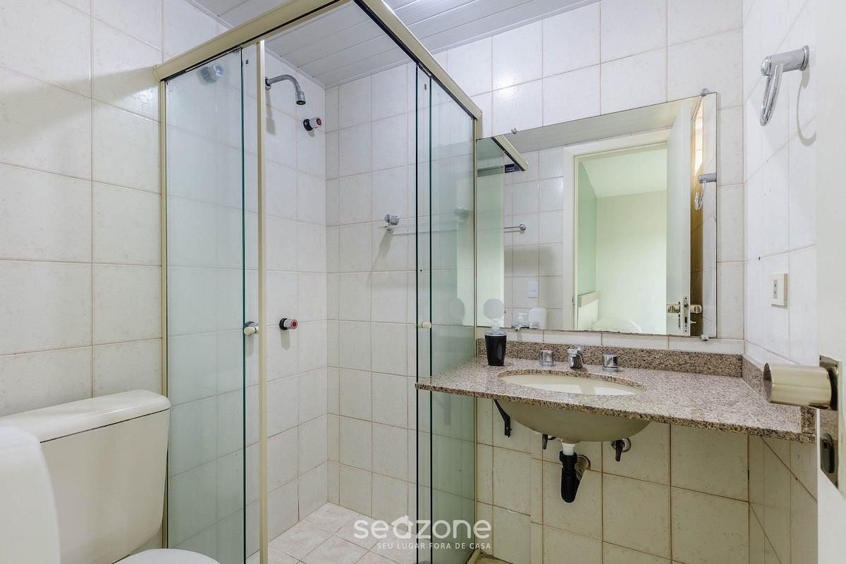 Een badkamer met een douchecabine van glas, een wastafel met een granieten blad en een spiegel boven de wastafel.