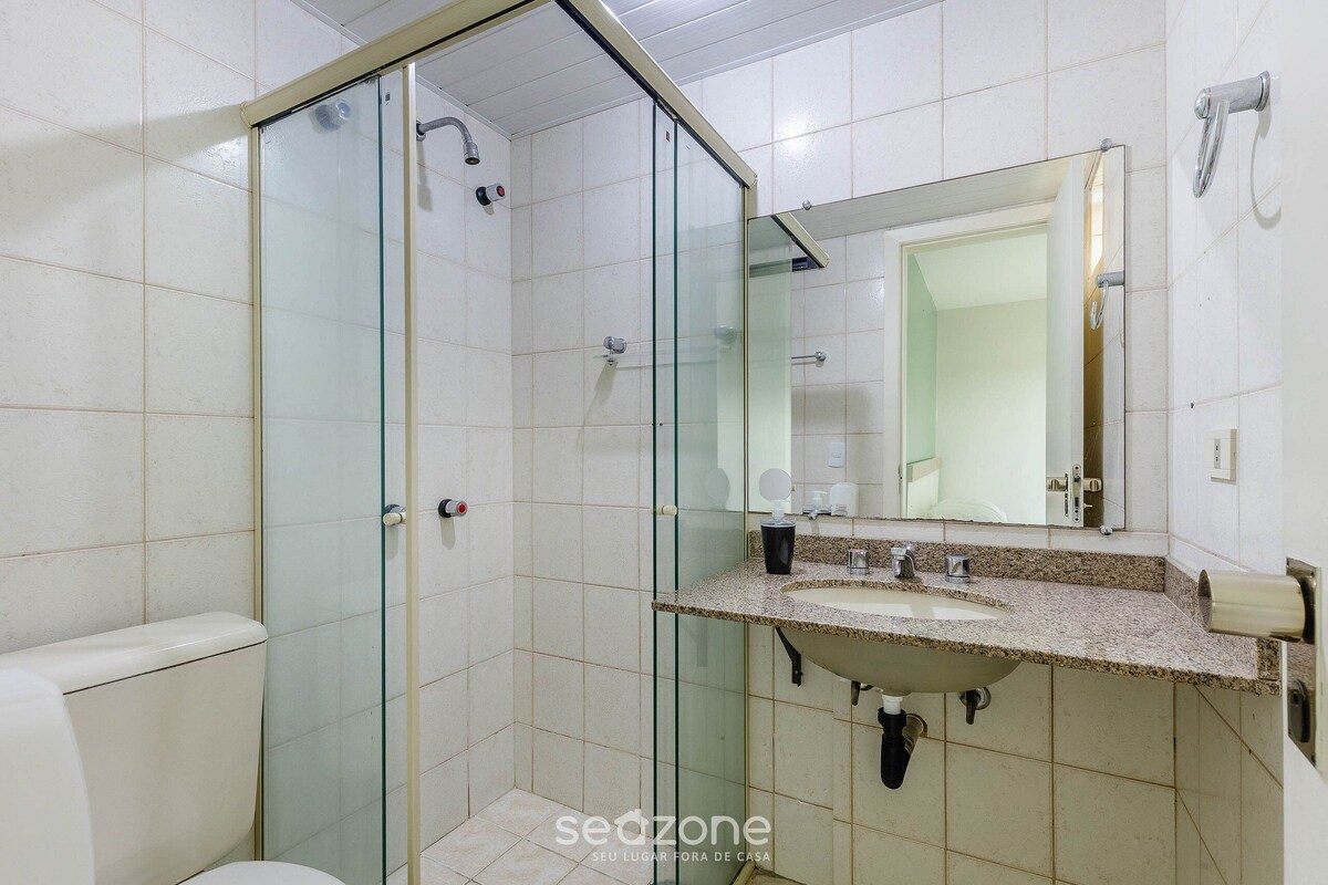 A bathroom with a glass shower enclosure, a sink with a granite countertop, and a mirror above the sink.
