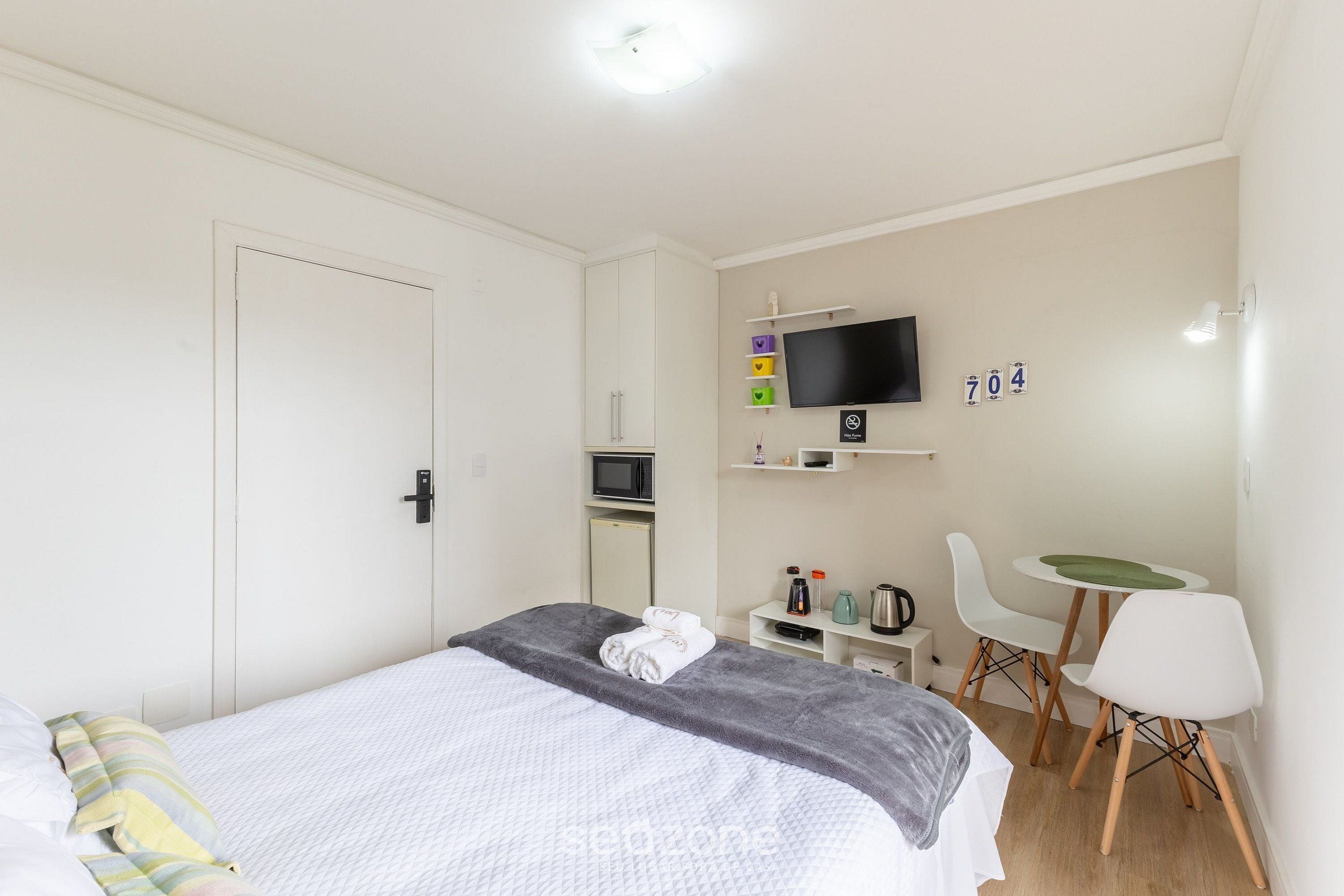 Ein Schlafzimmer mit einem Bett, einem Fernseher, einem Schreibtisch und einem Sessel.