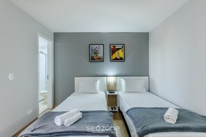 A hotel room with two beds, a nightstand with a lamp, and two framed artworks on the wall. - Studios at Upper Residence - UPP (Curitiba)
