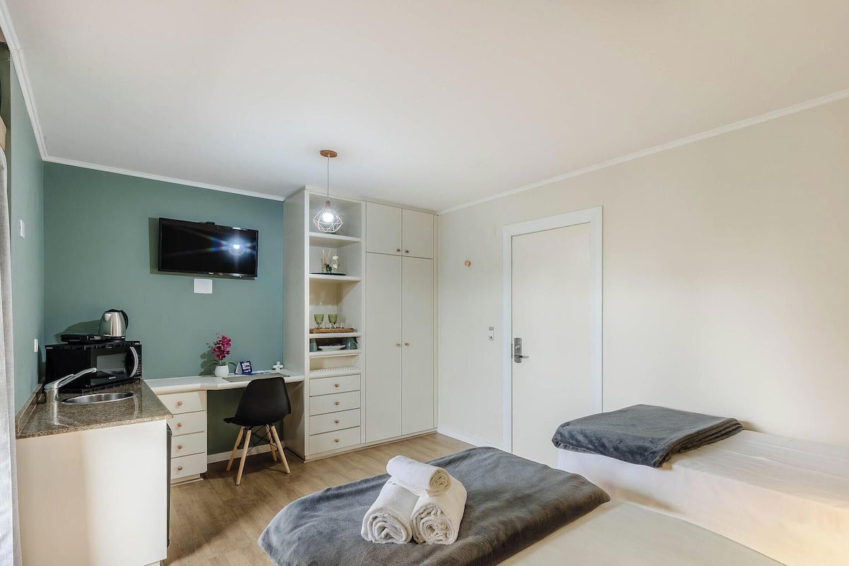 Een slaapkamer met een bed, een bureau met een computer, een televisie en een kledingkast.