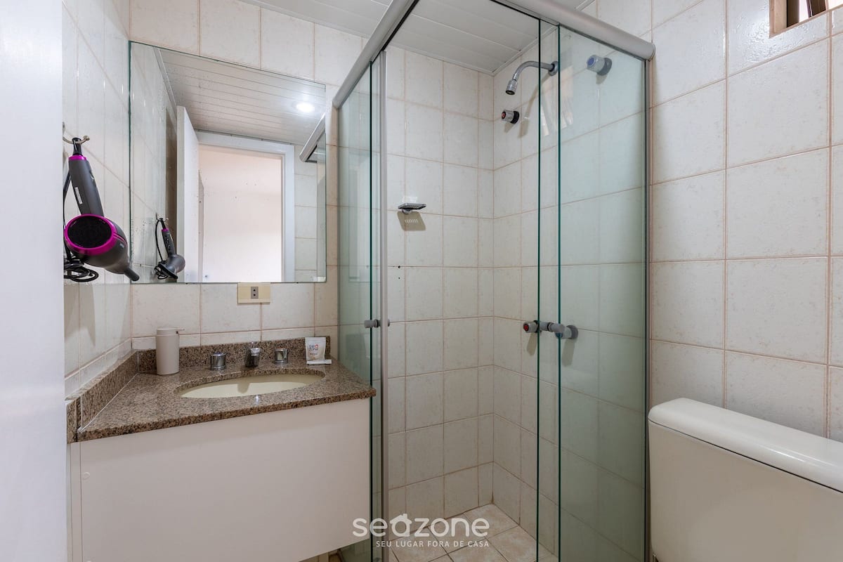 Een badkamer met een douchecabine van glas, een wastafel met een granieten aanrechtblad en een spiegel boven de wastafel.
