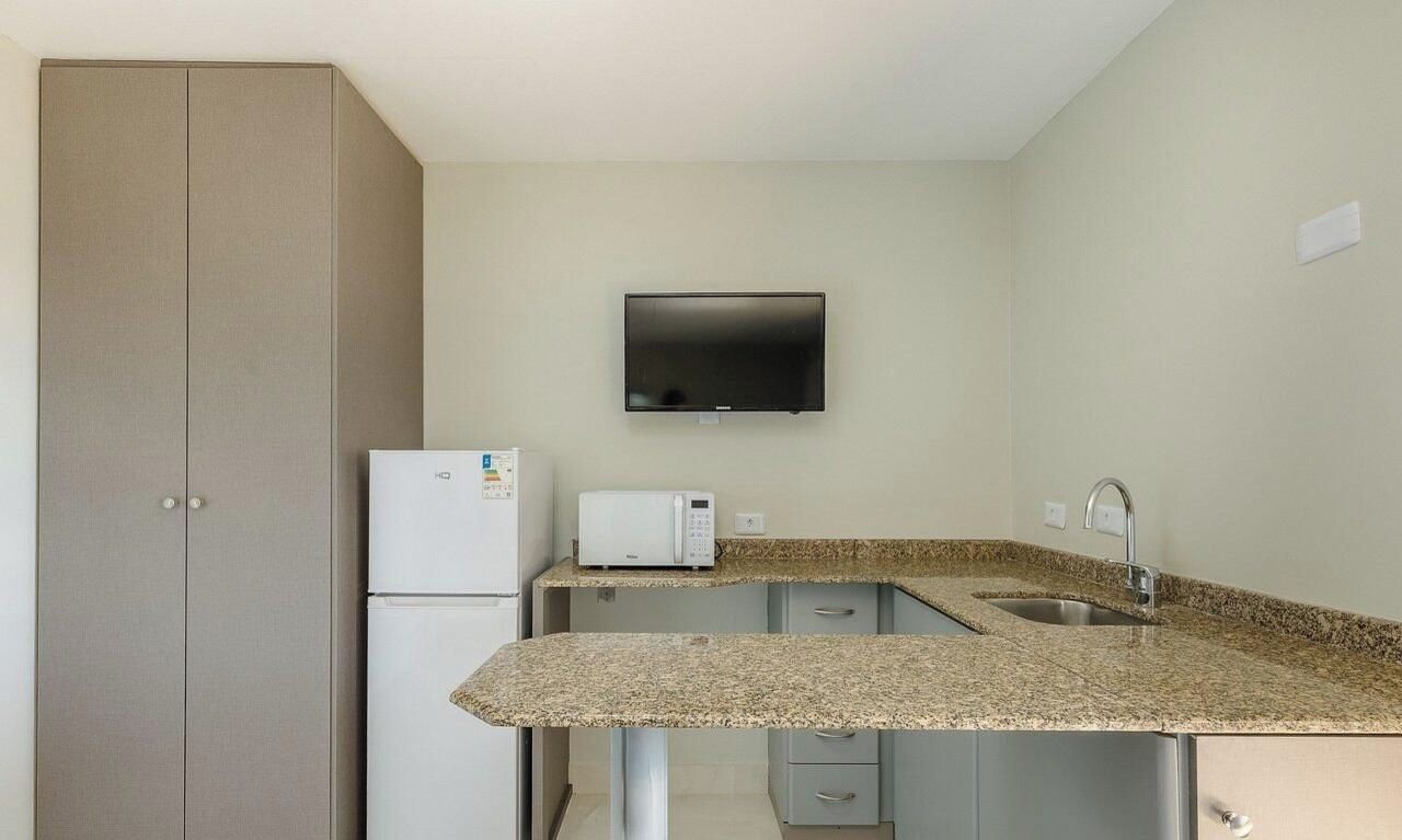 A compact kitchen with a microwave, toaster, and a flat-screen TV mounted on the wall.