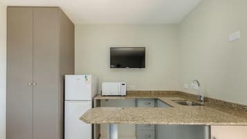 A compact kitchen with a microwave, toaster, and a flat-screen TV mounted on the wall.