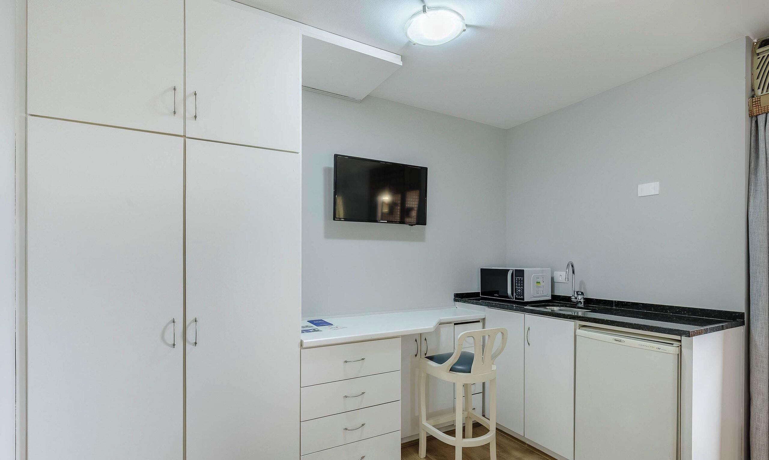 A compact kitchen with white cabinets, a black countertop, a microwave, a sink, and a chair.