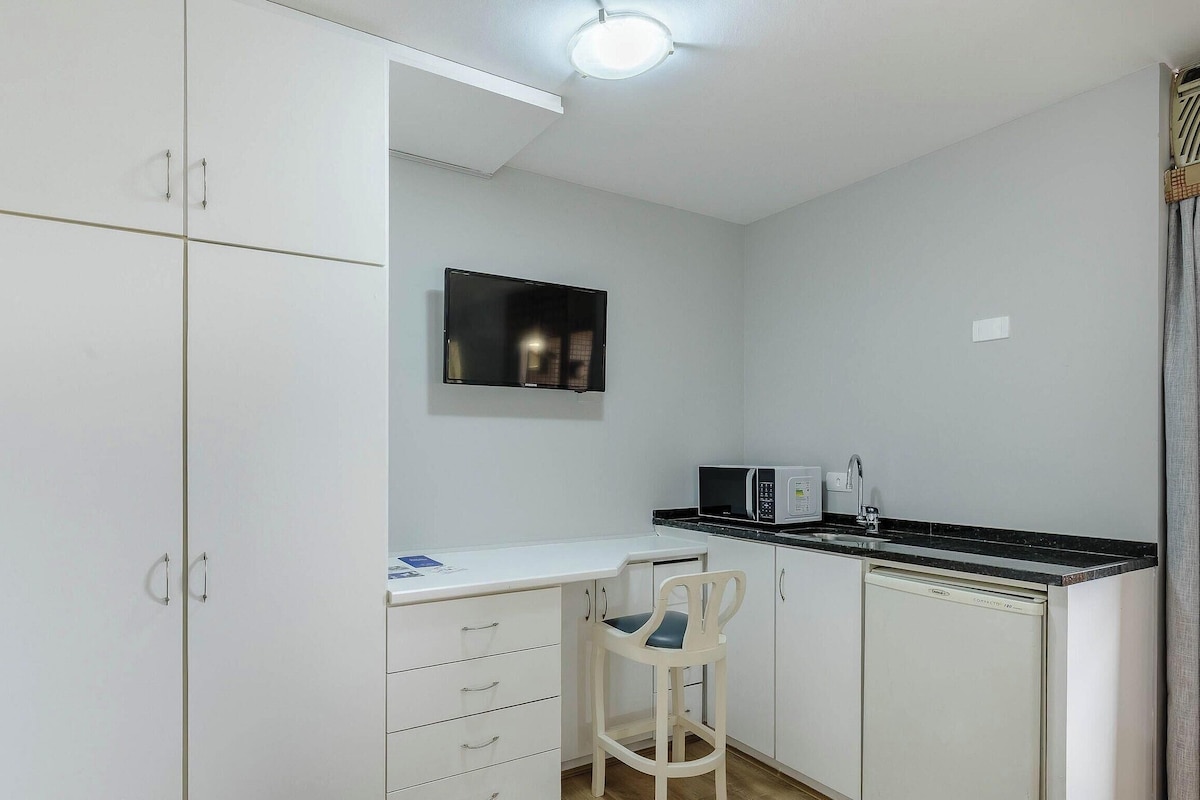 A compact kitchen with white cabinets, a microwave, a sink, and a chair.
