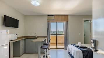 Habitación de hotel compacta con kitchenette, cama, televisor y balcón con vistas.