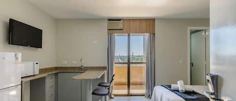 A compact hotel room with a kitchenette, a bed, a TV, and a balcony with a view.