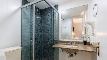 Un baño con cabina de ducha de vidrio, lavamanos con espejo y secador de pelo en la pared.