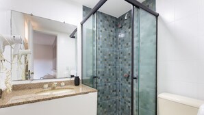Een badkamer met een glazen douchecabine, een granieten aanrechtblad en een wit toilet.