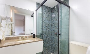 A bathroom with a glass shower enclosure, a granite countertop, and a white toilet.