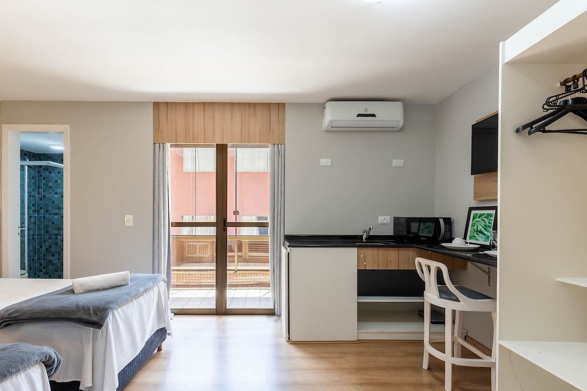 Een kleine kamer met een bed, bureau, stoel en kitchenette.
