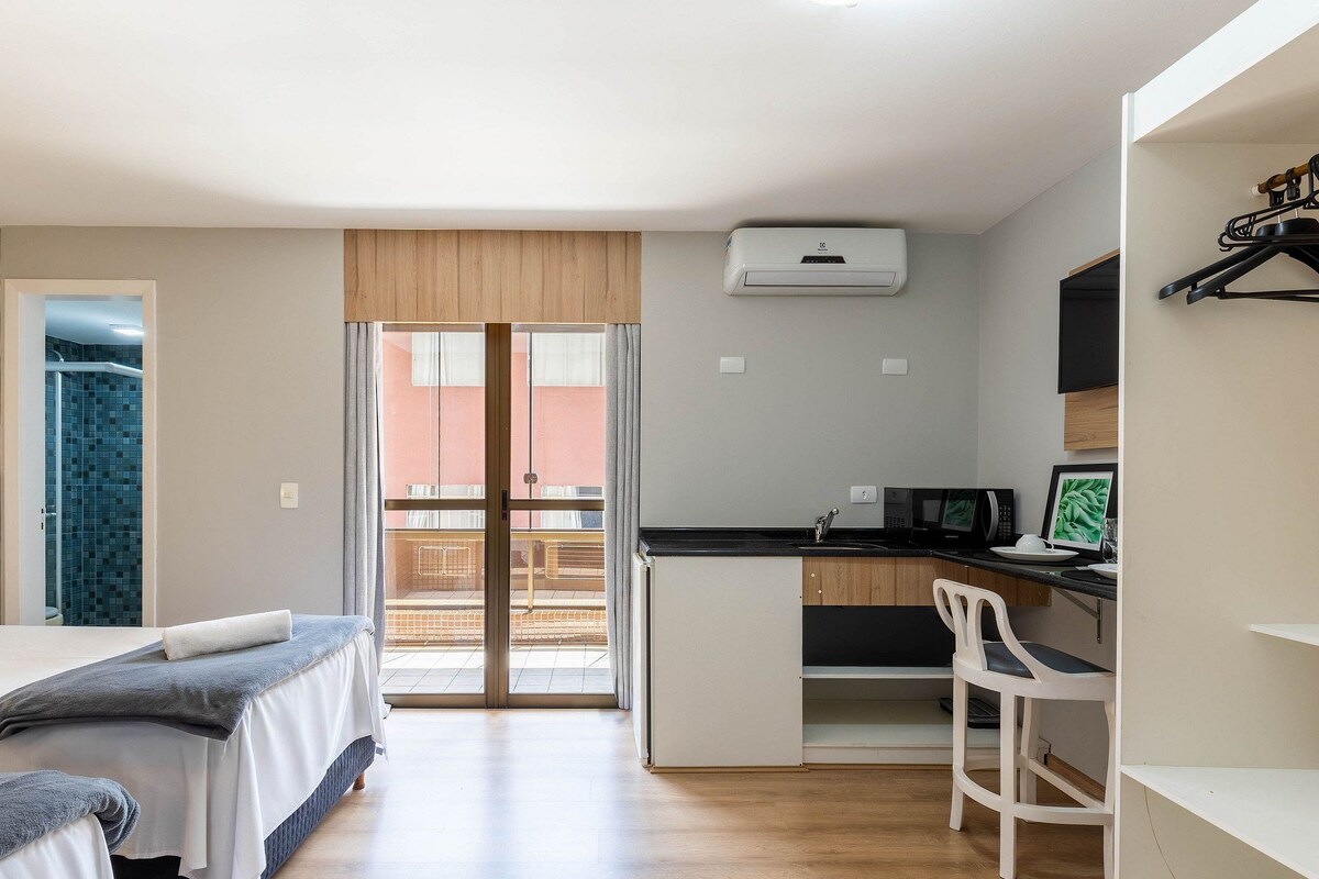 Een kleine kamer met een bed, bureau, stoel en kitchenette.