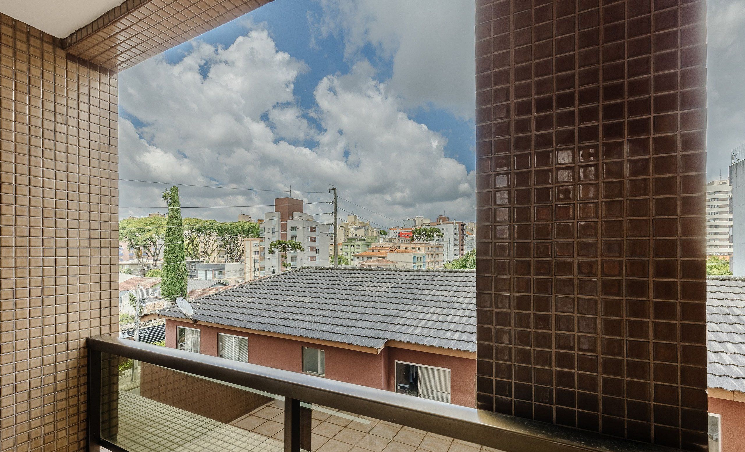 A residential building with a tiled roof, a balcony with a metal railing, and a view of the cityscape.