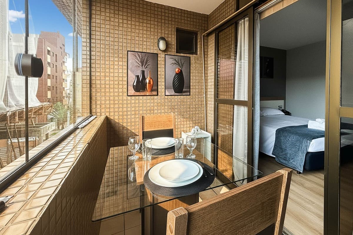 Een balkon met een tafel voor twee, een bed in de aangrenzende kamer en uitzicht op de stad.