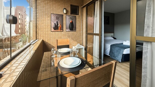 Een balkon met een tafel voor twee, een bed in de aangrenzende kamer en uitzicht op de stad.