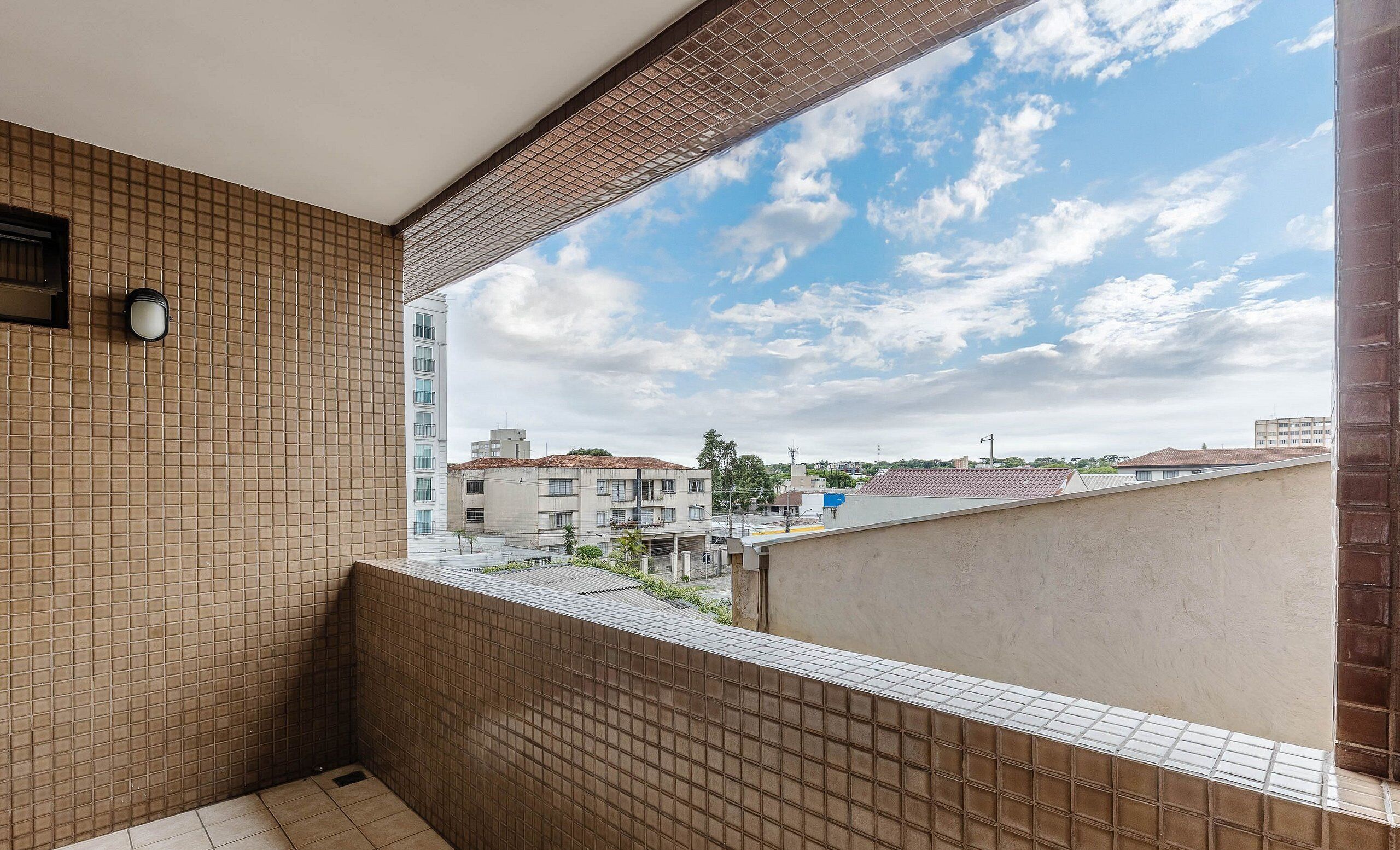 A balcony with a tiled wall, a view of buildings, and a clear sky.