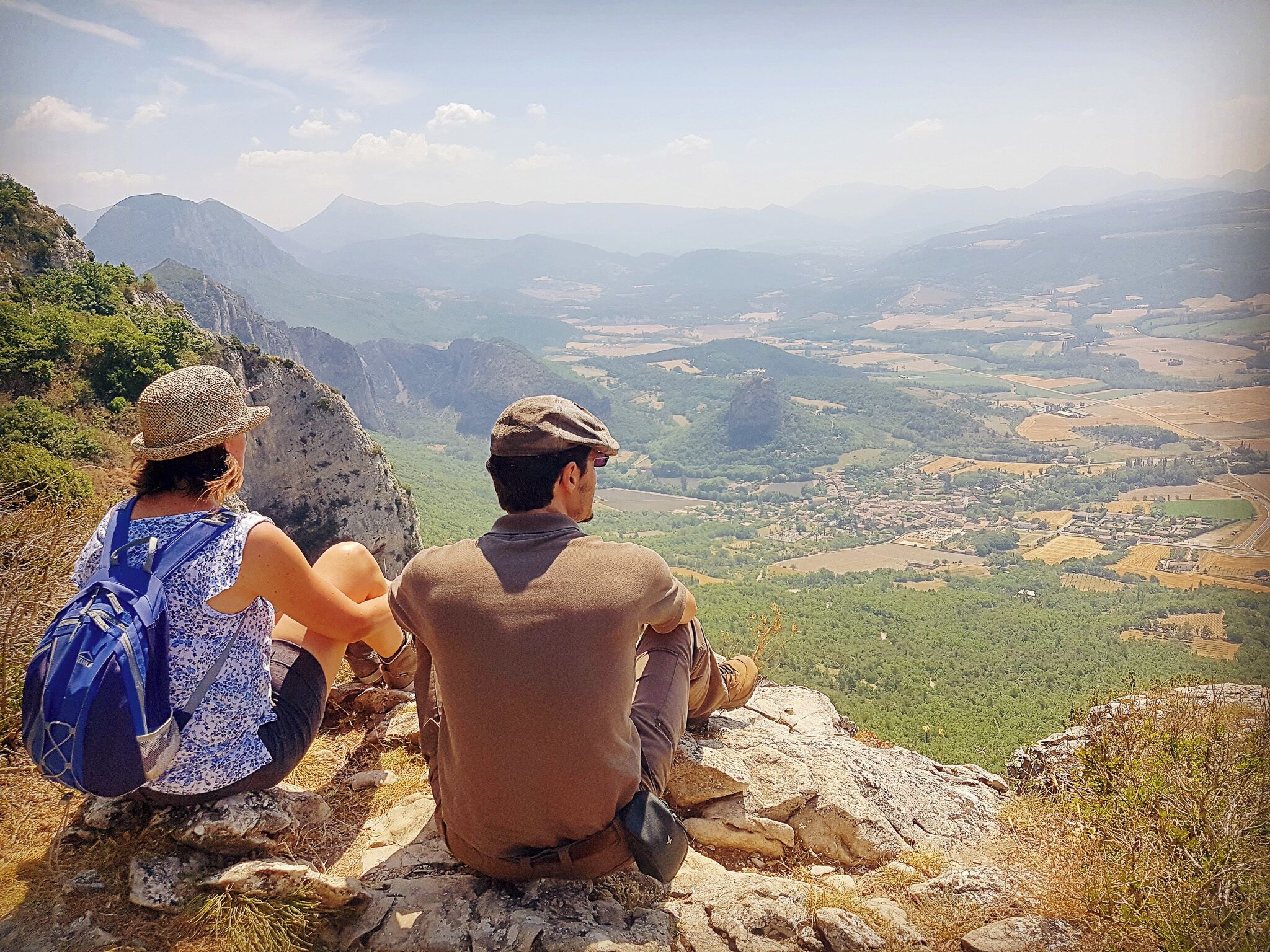 Zwei Personen sitzen auf einem Felsen mit Blick auf ein Tal und Berge in der Ferne.