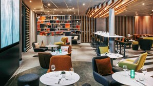 A modern restaurant with round tables, chairs, and a bar area. - Novotel Paris Coeur D'orly (Orly)