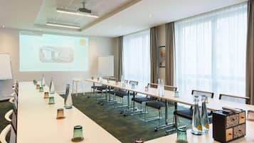 A conference room with a long table, chairs, a projector screen, and a large window with curtains.
