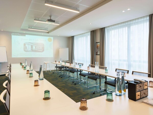 A conference room with a long table, chairs, a projector screen, and a large window with curtains.