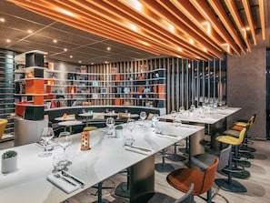 A modern restaurant with multiple dining tables, bar stools, and a variety of decorative items on shelves. - Novotel Paris Coeur D'orly (Orly)