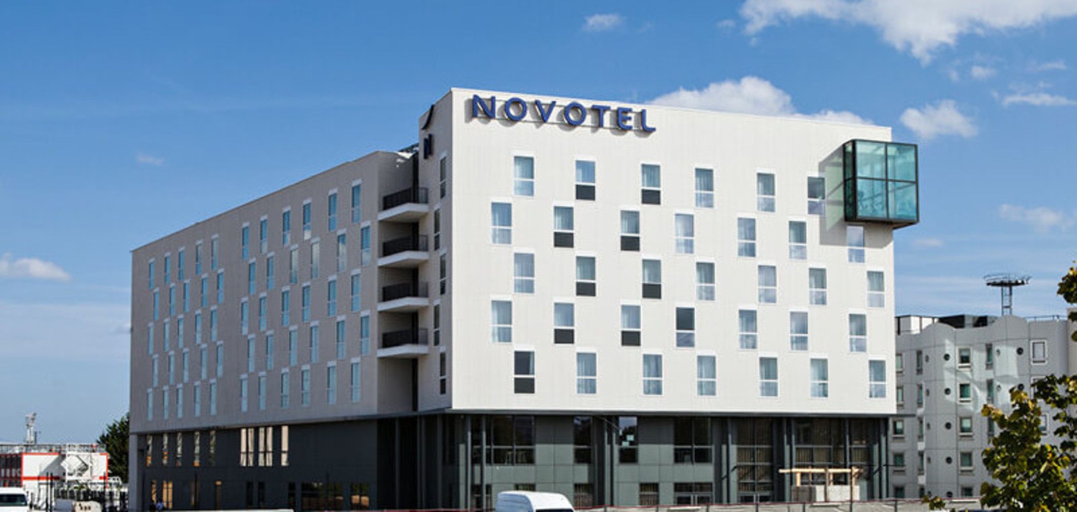 A modern hotel with a white facade, multiple floors, and a prominent 'NOVOTEL' sign.