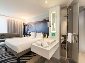 Una habitación de hotel moderna con una cama, un baño con espejo y lavabo, y una ducha.