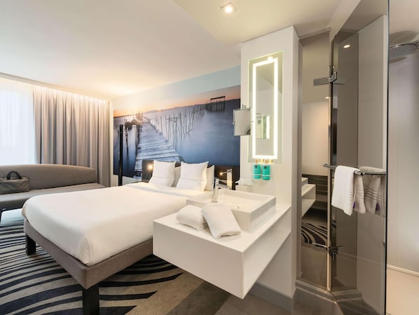 Habitació d'hotel moderna amb llit, bany amb mirall i rentapisa, i dutxa.
