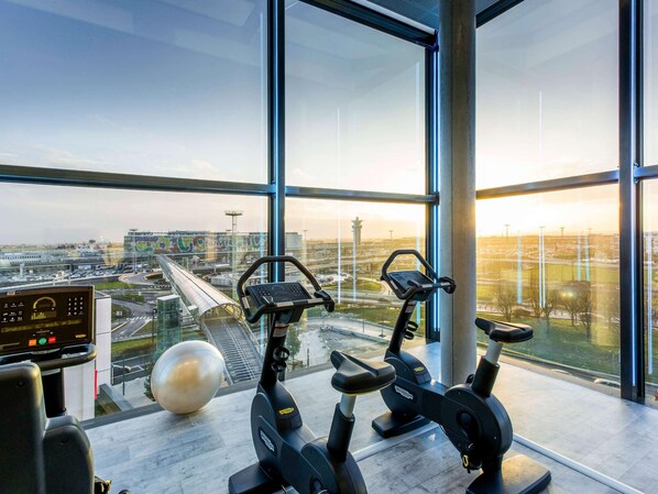Un gimnasio con equipo de ejercicio y un amplio ventanal con vistas al aeropuerto.