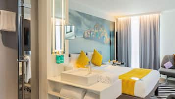 A modern hotel room with a large bed, a white vanity with a mirror, a painting on the wall, and a view of the city.