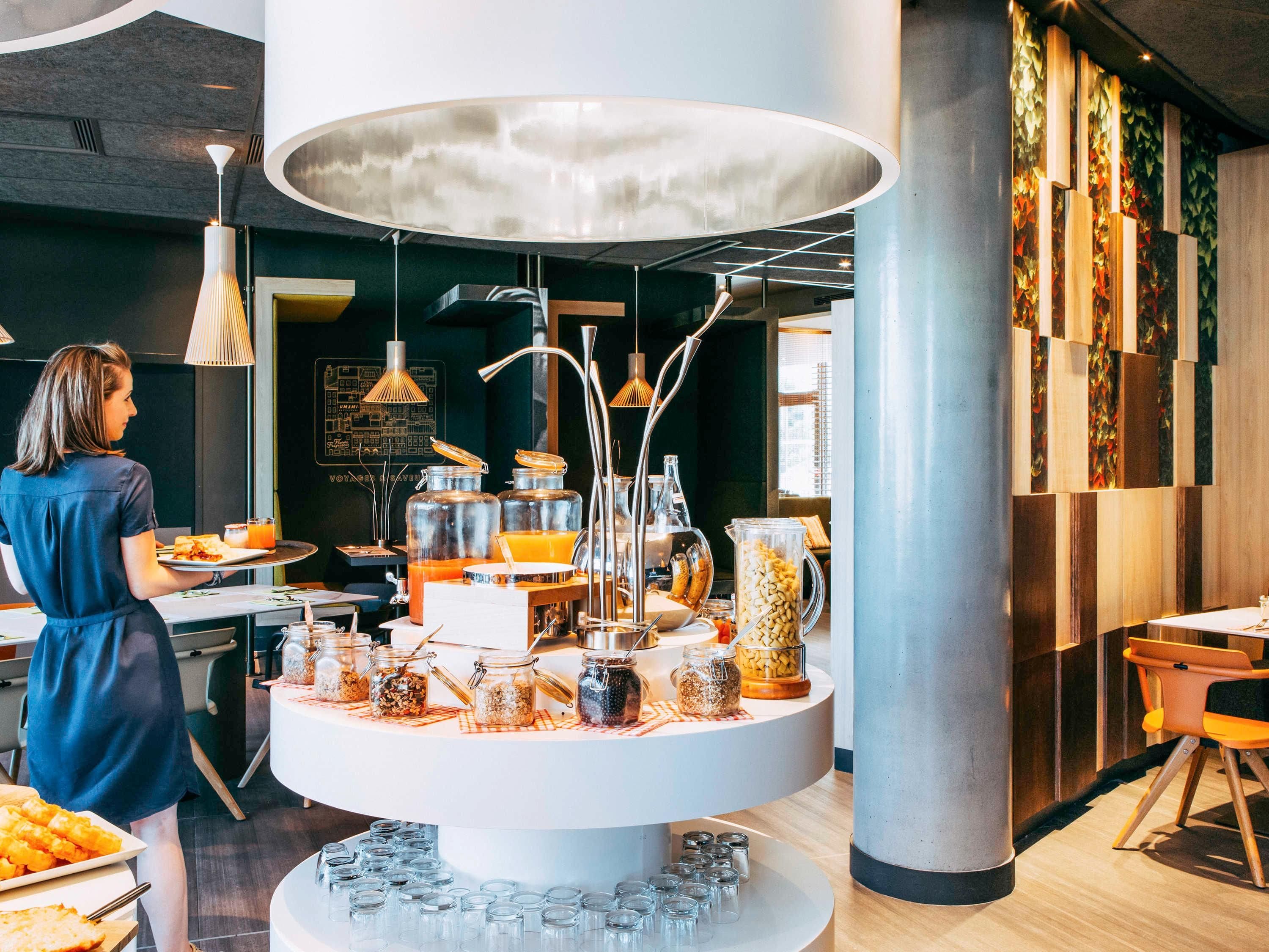Un bufé de desayuno con diversos alimentos y bebidas, un elemento decorativo central de iluminación y un diseño de interiores moderno.