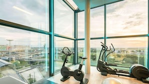 A gym with exercise equipment and a ping pong table, large windows with a city view. - Novotel Paris Coeur D'orly (Orly)