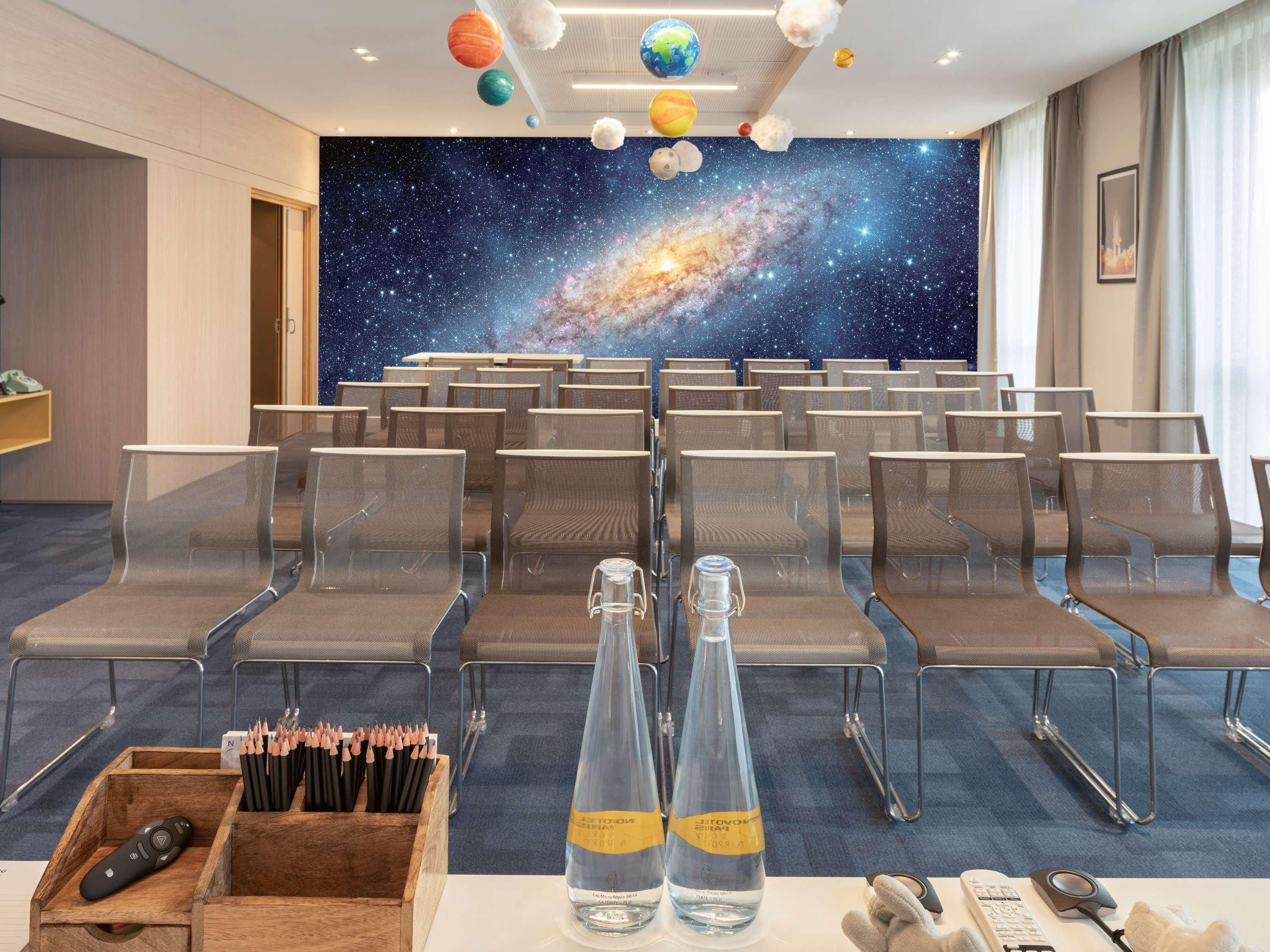 A conference room with rows of chairs, a galaxy-themed wall mural, and a wooden box with pencils and a remote control.