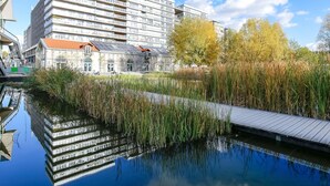 A modern building with a reflective water body in front, a wooden deck, and a clear sky. - Novotel Paris Coeur D'orly (Orly)