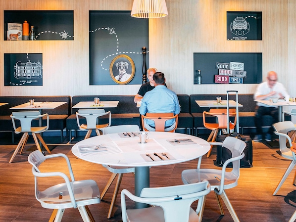Un restaurant amb taules rodones, cadires i una paret amb quadres i text emmarcats.
