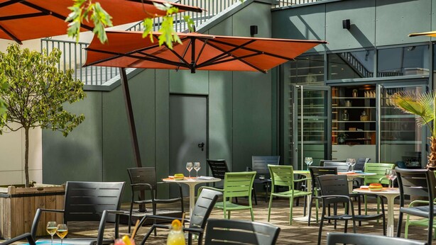 An outdoor seating area with tables and chairs, a staircase, and a building with large windows. - Novotel Paris Coeur D'orly (Orly)