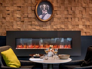 A modern interior with a wooden wall, a framed picture, a fireplace, and a dining setup.