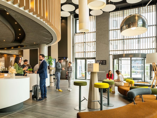 A modern hotel lobby with a curved reception desk, seating areas, and large windows. - Novotel Paris Coeur D'orly (Orly)
