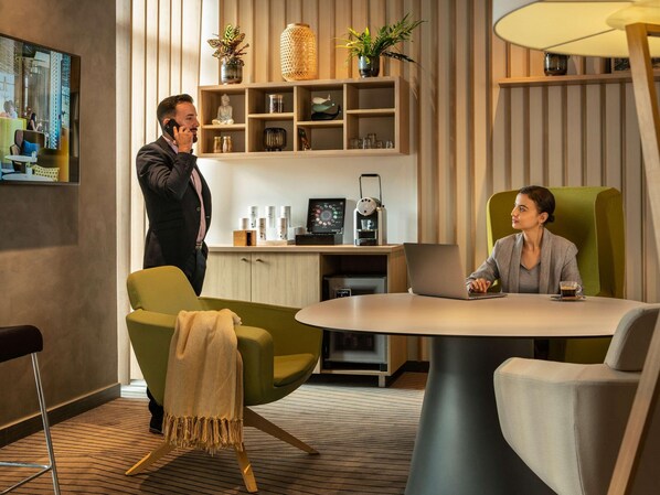 Habitación de hotel moderna con una mesa redonda, dos sillas, una cafetera y un estante con objetos decorativos.
