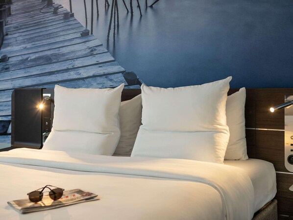 A modern hotel room with a wooden staircase, a bed with white bedding, and a nightstand with a lamp. - Novotel Paris Coeur D'orly (Orly)