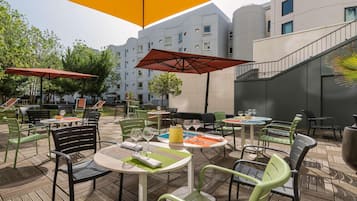 Un patio al aire libre con mesas y sillas, sombrillas y un edificio al fondo.