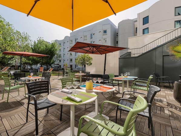 Un patio al aire libre con mesas y sillas, sombrillas y un edificio al fondo.