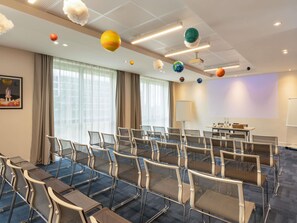 Un salón de conferencias con filas de sillas, una pantalla de proyector y un espacio para presentaciones.