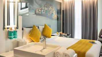 Habitación de hotel con una cama grande, un lavamanos blanco, un espejo y un cuadro en la pared.