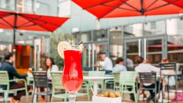 A table with a tall glass of red drink, a lemon slice, and a small bowl of food.