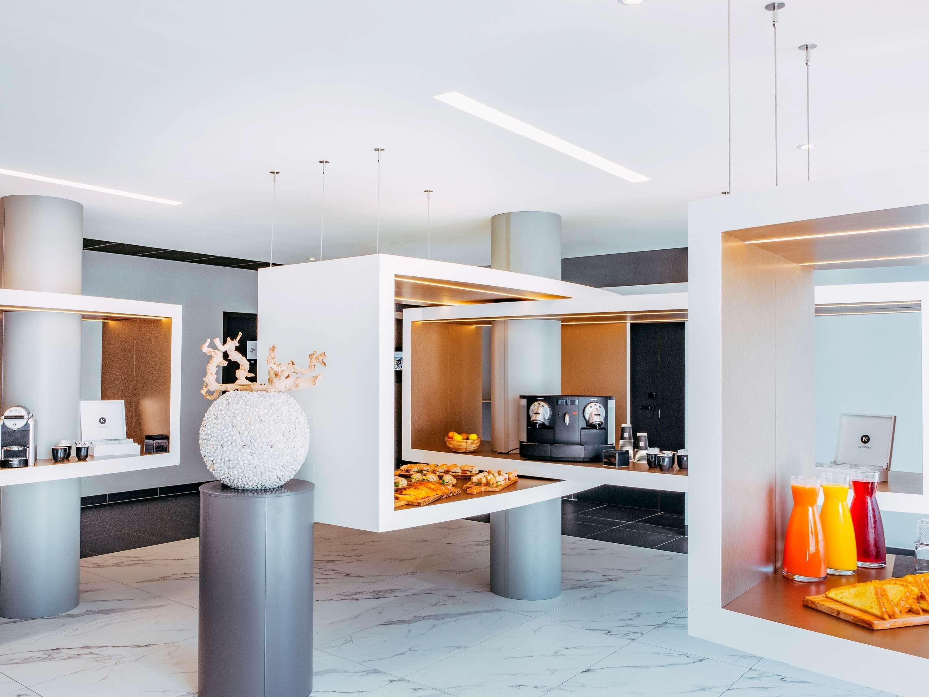 Un vestíbulo de hotel moderno con un mostrador de recepción, máquinas de café y una exposición de fruta.